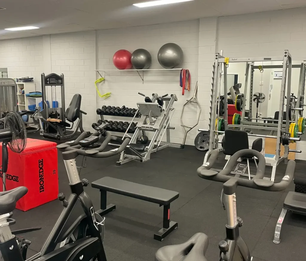 Fully equipped strength and conditioning gym at Complete Physio Richmond featuring squat racks, dumbbells, weight plates and exercise bikes used for bone health and rehabilitation programs