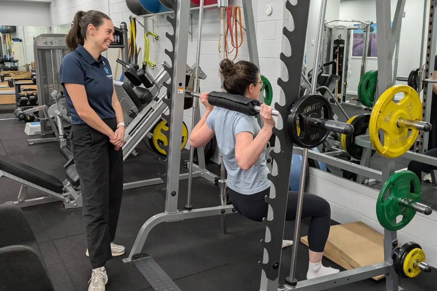 Physiotherapist supervising a patient performing a barbell squat during an exercise rehabilitation session
