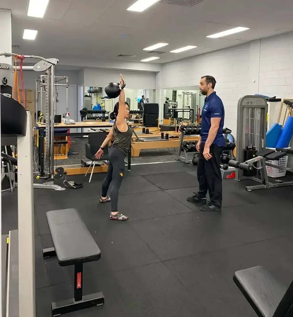 Client pressing a kettlebell overhead while a strength and conditioning coach observes at Complete Physio Richmond