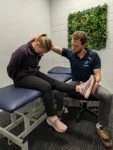 Physiotherapist guiding a patient through a seated low back pain assessment and leg stretch at Complete.